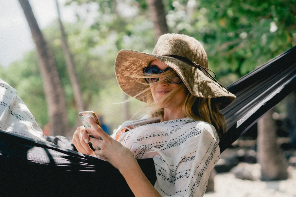 Une femme assise dans un hamac au soleil, portant un chapeau de soleil et des lunettes de soleil.